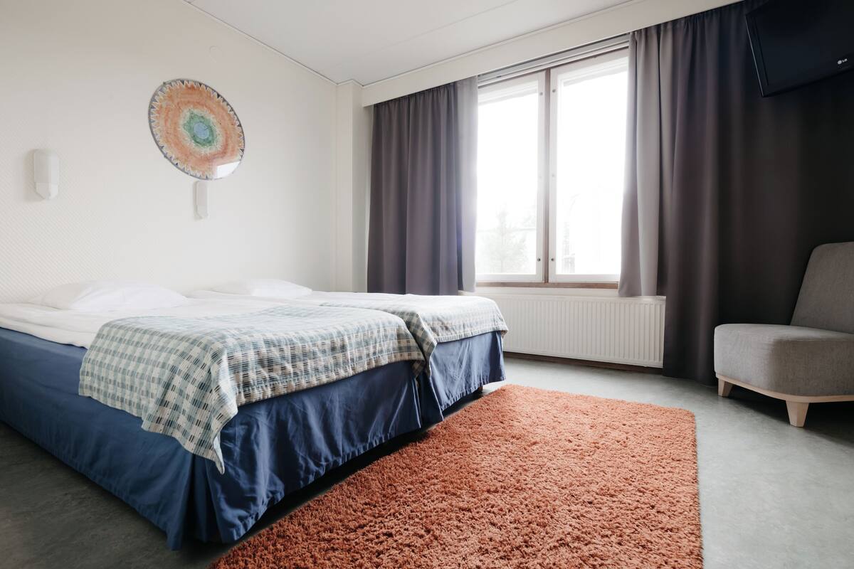 Una habitación de hotel moderna con cama, una silla, un ventanal con cortinas y una obra de arte colgada en la pared.