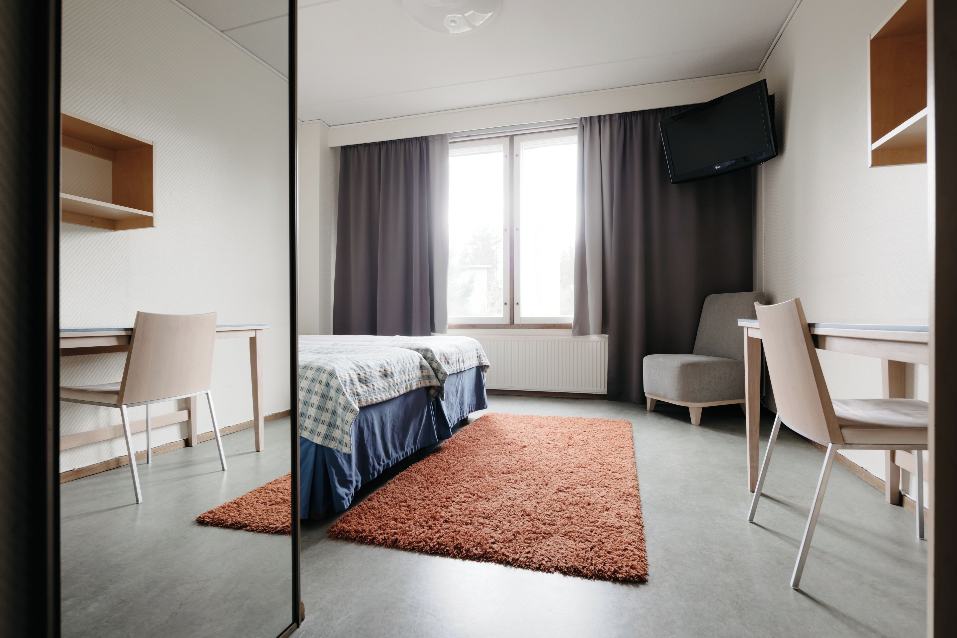 Una habitació d'hotel moderna amb un llit, dues cadires, un escriptori, una televisió i una finestra amb cortines.