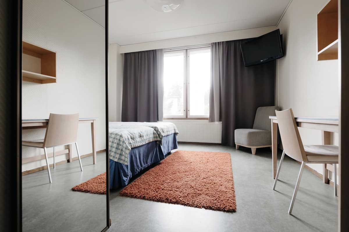 Una habitación de hotel moderna con una cama, dos sillas, un escritorio, un televisor y una ventana con cortinas.