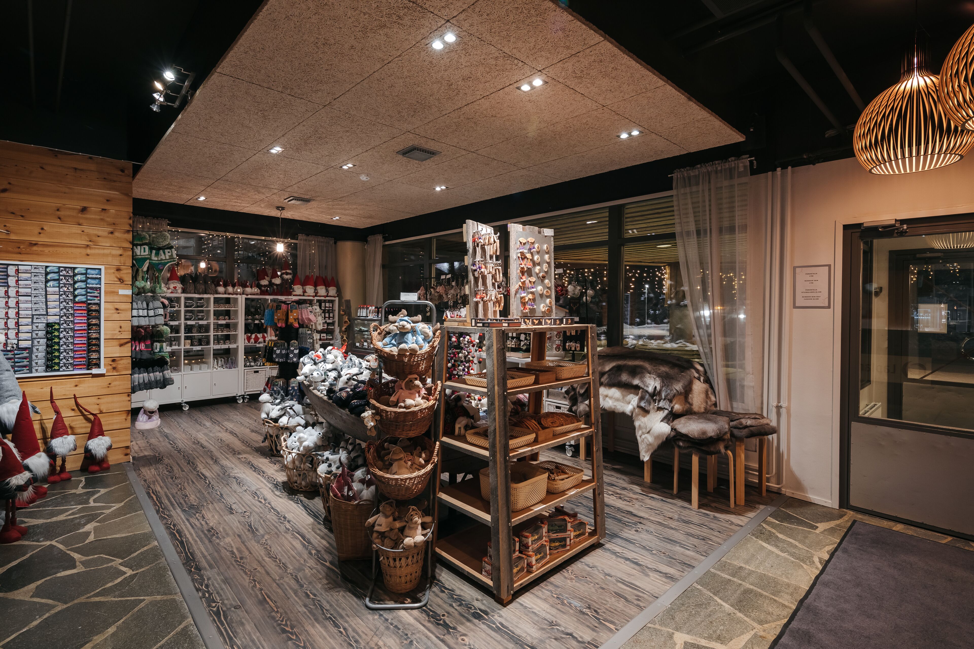 A cozy boutique hotel interior with wooden decor, a central display of baskets and plush toys, and a view of the city through large windows.