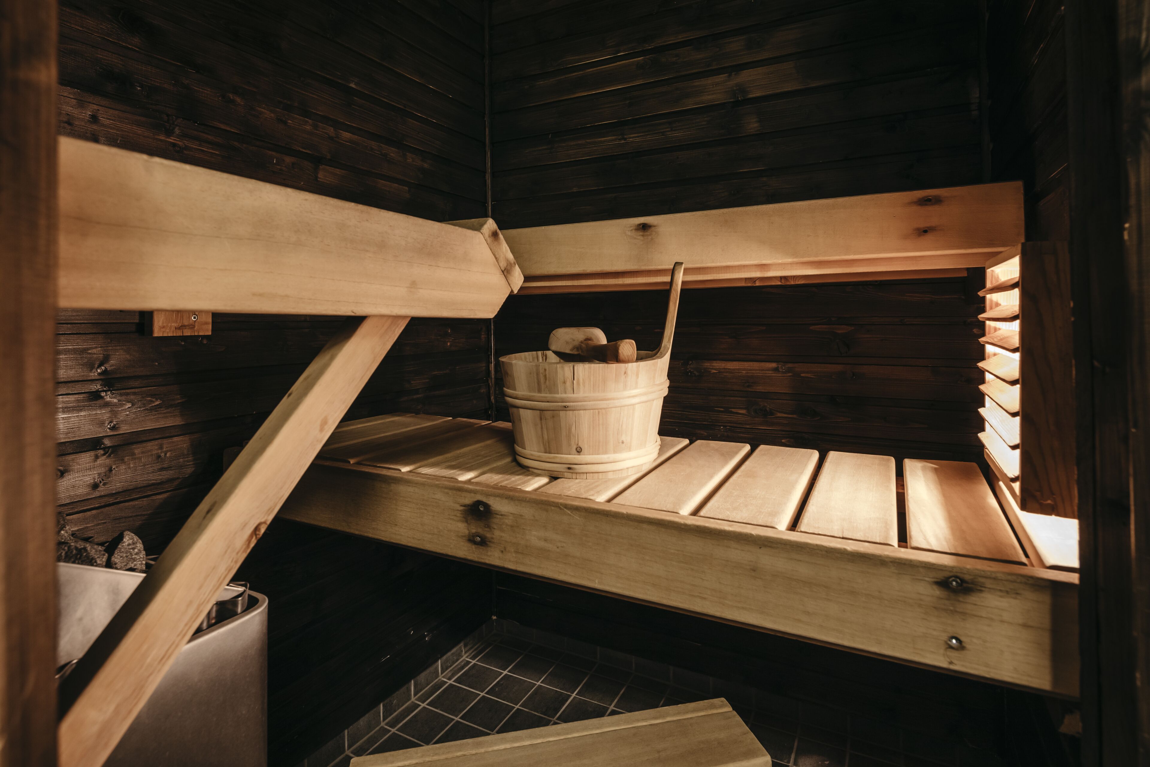 A wooden cabin with a bunk bed, a wooden bucket, and a metal container.