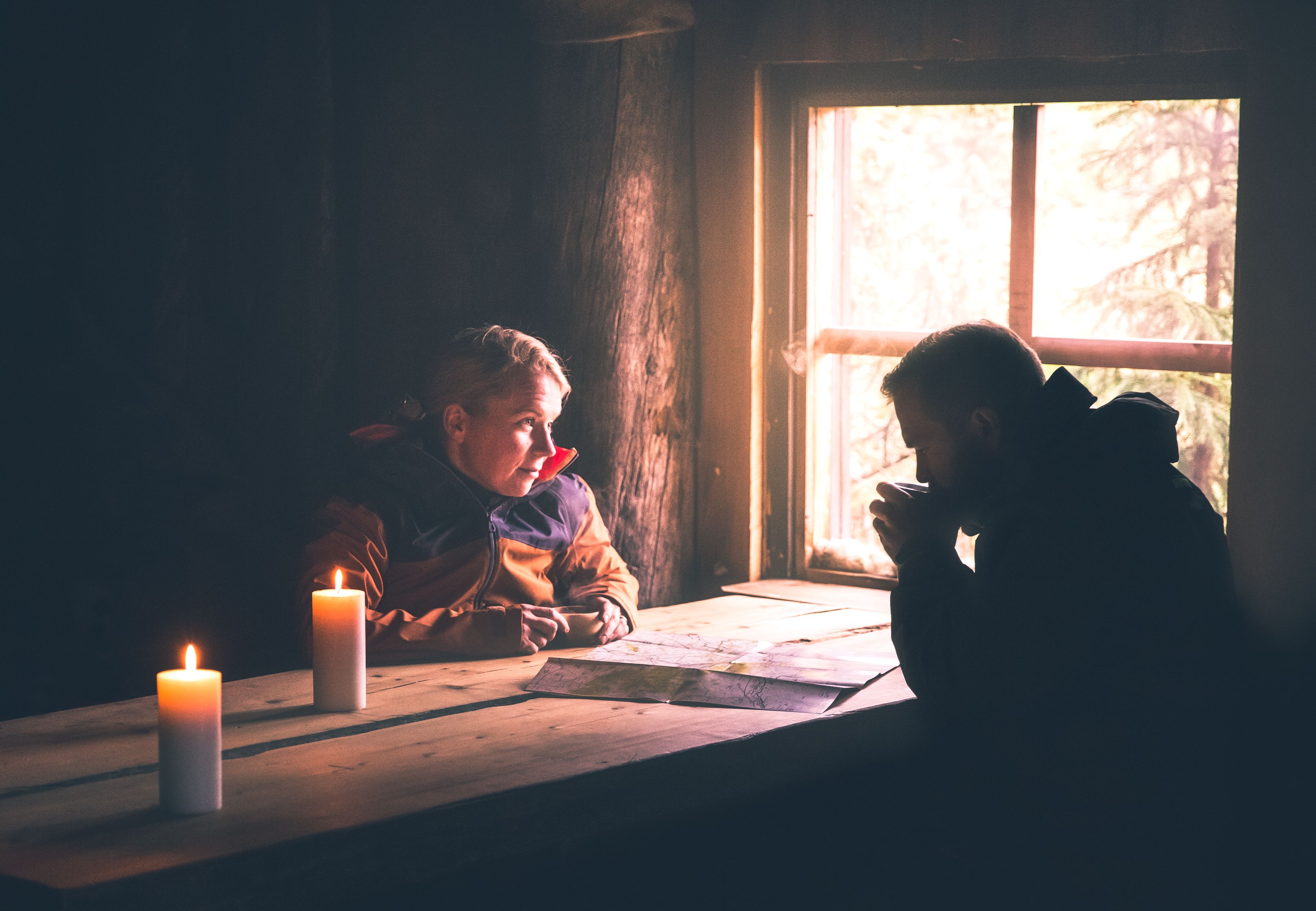 Dos niños sentados a una mesa de madera junto a una ventana con velas.