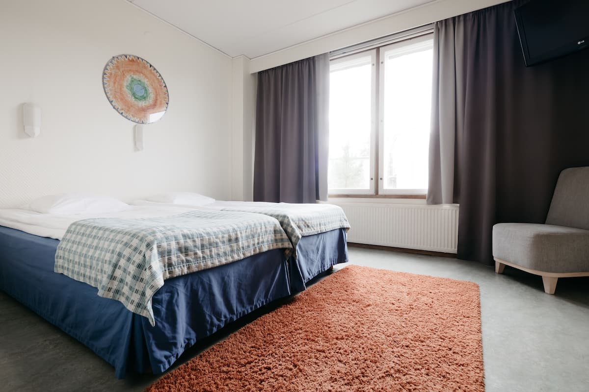 Una habitación de hotel moderna con cama, una silla, un ventanal con cortinas y una obra de arte colgada en la pared.