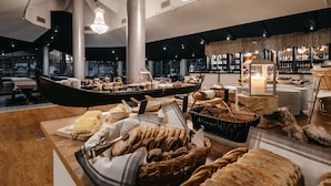 A buffet setup with various breads and cheeses, a boat-shaped serving table, and a bar area with bottles in the background. - Lapland Hotels Ylläskaltio (Kolari)