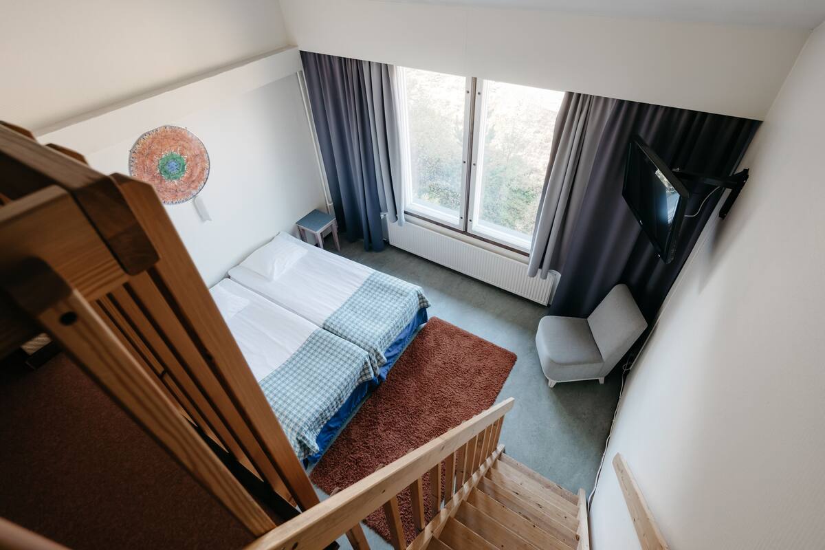 Un dormitorio con cama, una silla, televisión y ventana con cortinas.