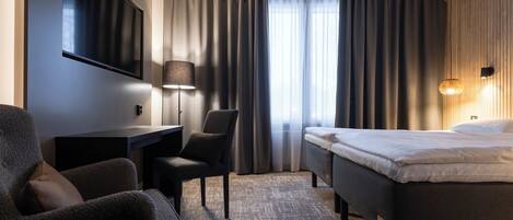 A hotel room with a bed, a desk, a chair, a TV, and a window with curtains.