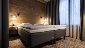 A modern bedroom with a wooden ceiling, a bed with grey bedding, two wall-mounted lights, and a window with curtains. - Lapland Hotels Ylläskaltio (Kolari)