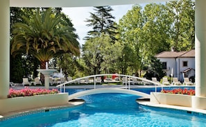 A pool area with lounge chairs and a bridge over the water, surrounded by trees and a building. - Hotel Dos Templarios (Tomar)