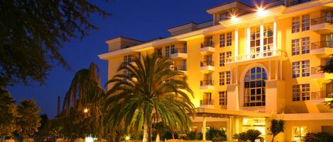 A multi-story hotel with a central courtyard, palm trees, and a well-lit entrance.