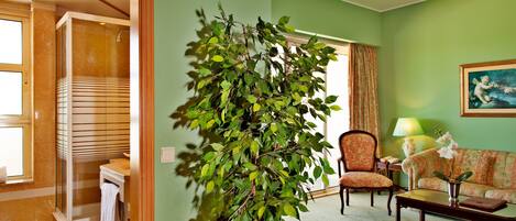A hotel room with a bathroom, a living area with a sofa, a coffee table, and a potted plant.