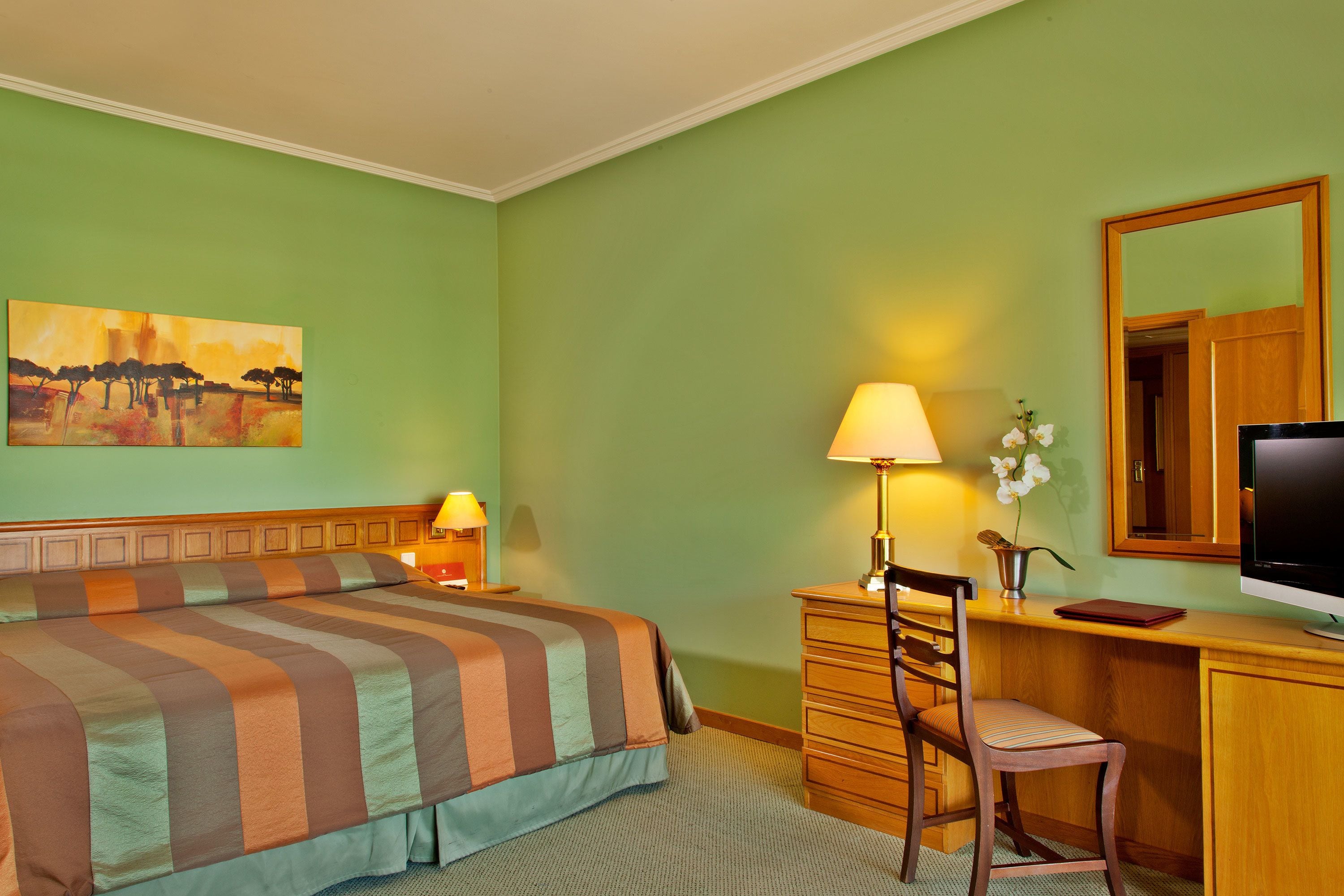 Habitació d'hotel amb llit, escriptori, cadira, làmpada, televisió i un quadre a la paret.