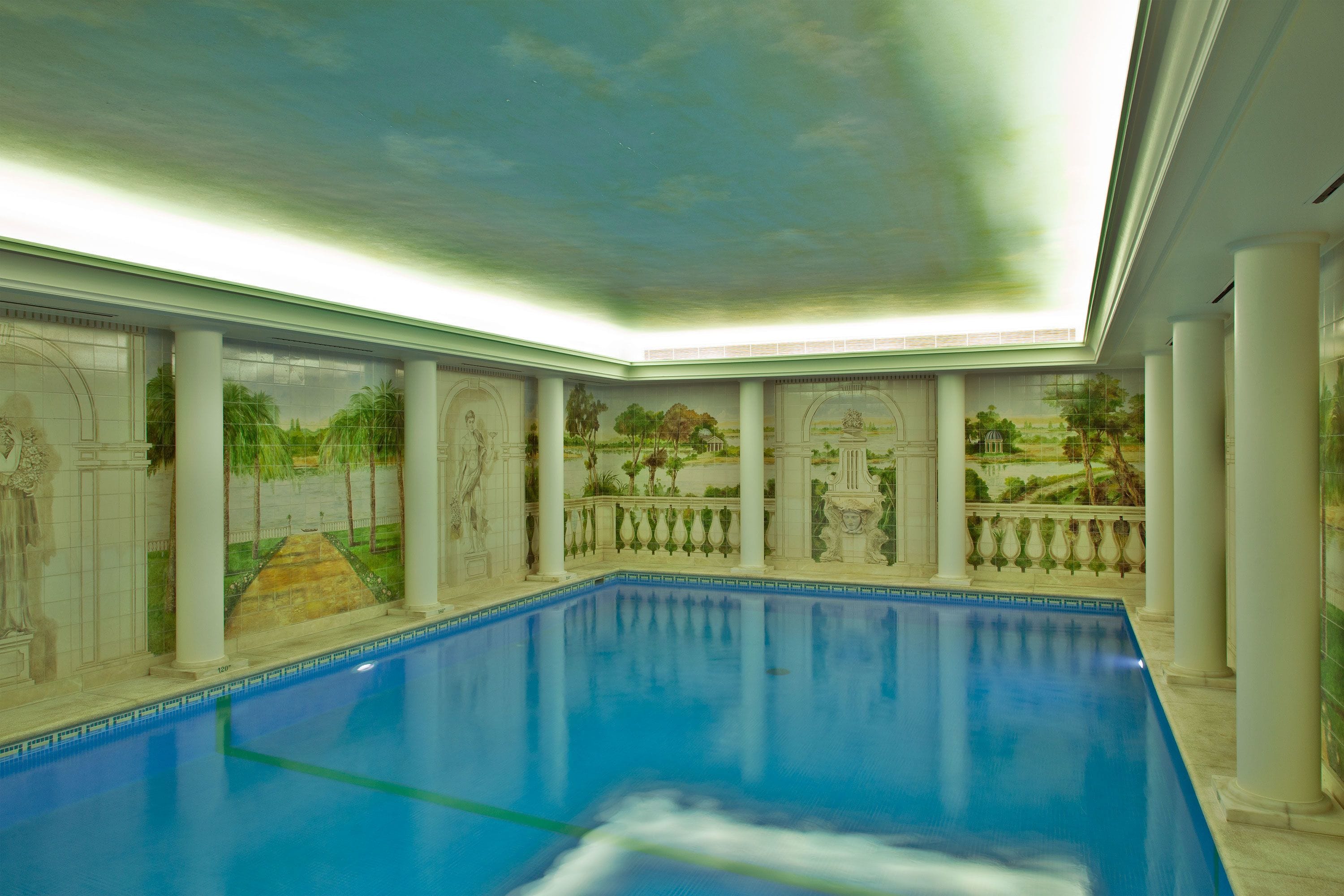 Une piscine intérieure dont les murs sont ornés d’une fresque représentant un paysage.