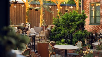 An outdoor patio with wicker furniture, brick walls, and hanging plants.