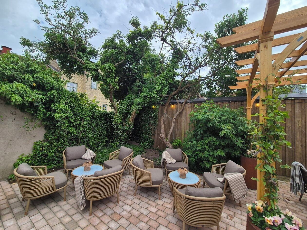 Een terras met rieten meubels, een houten pergola en een betegelde vloer.