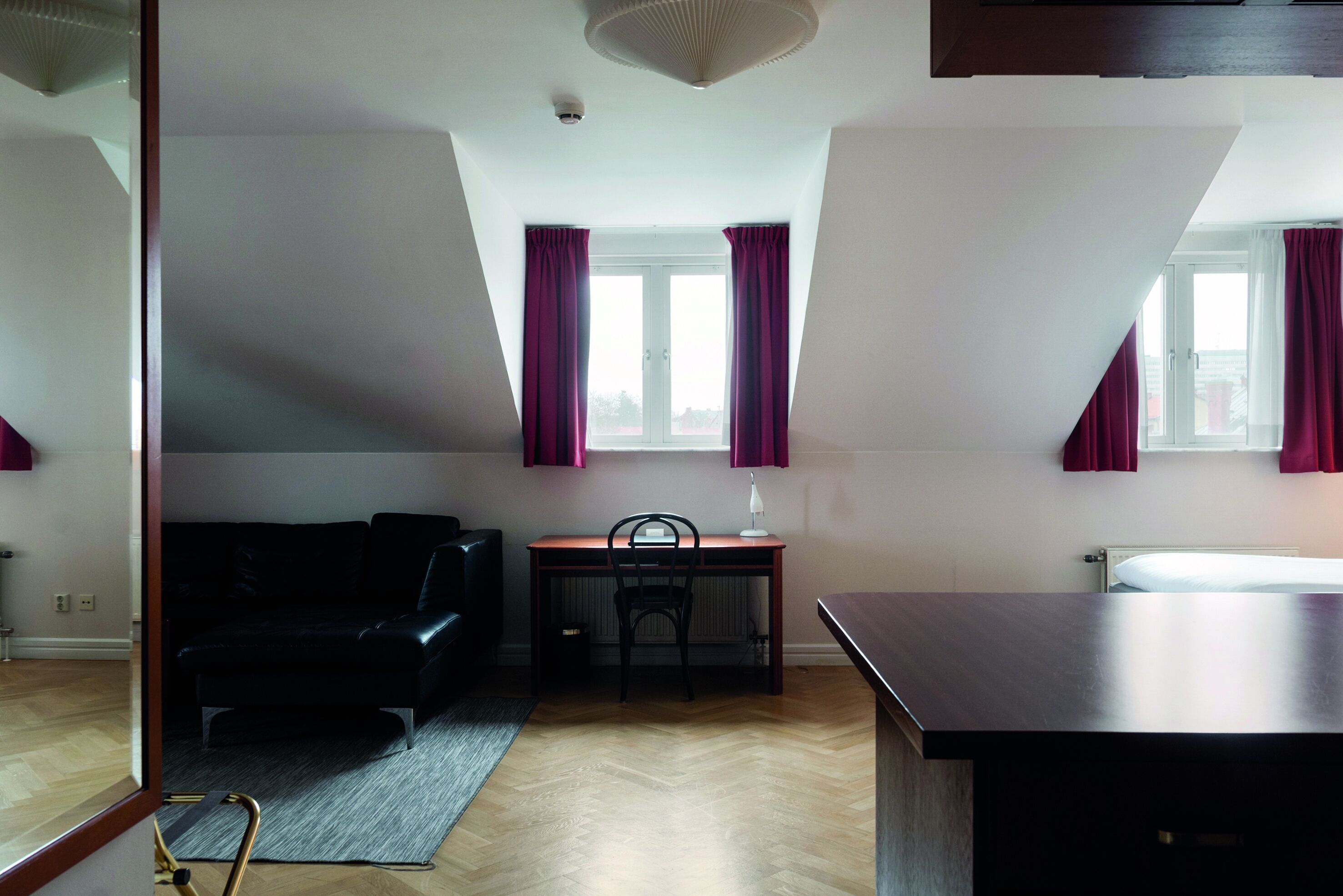 Una habitación con piso de madera, un sofá negro, un escritorio con una silla y una cama.