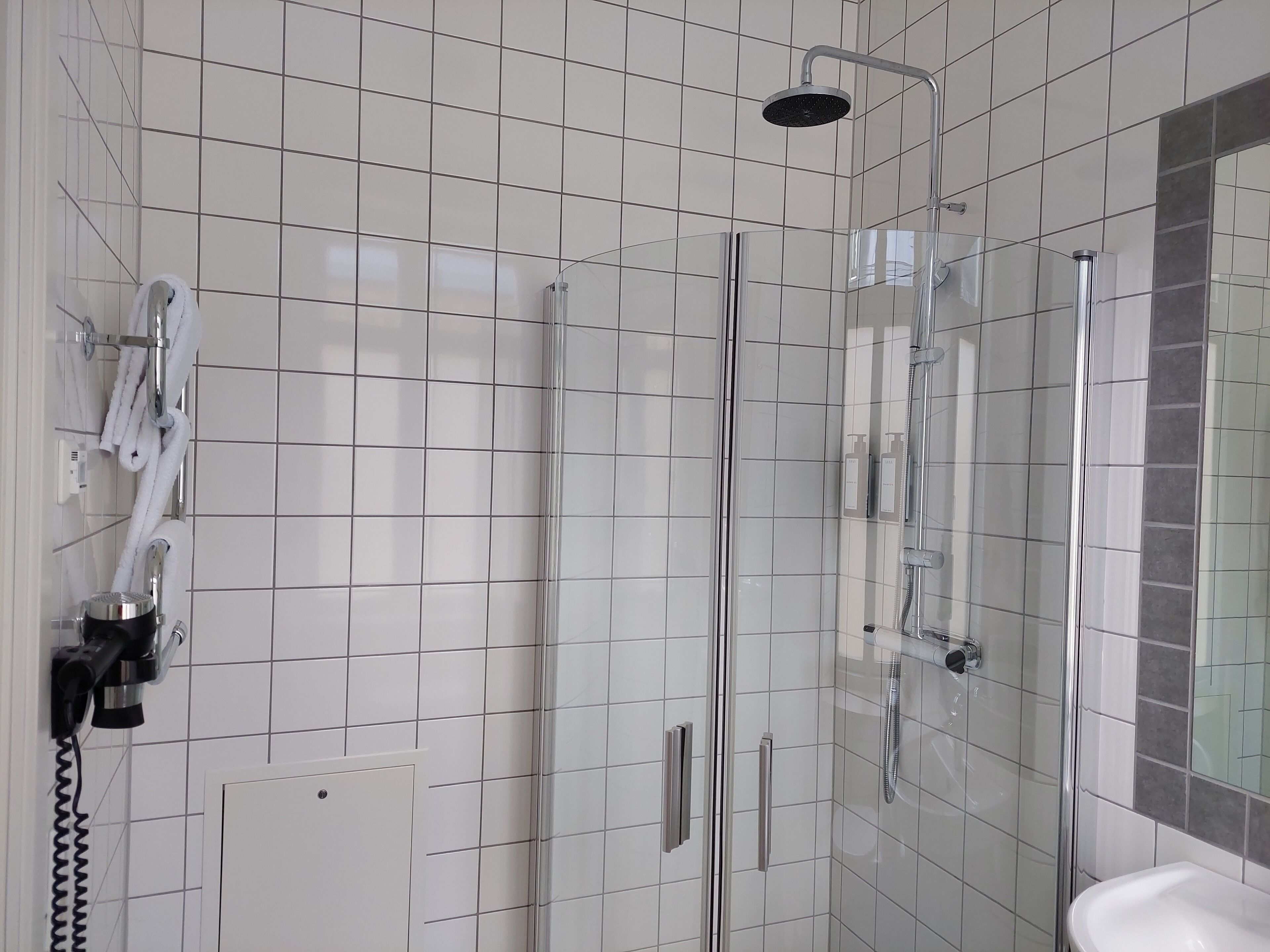 Une salle de bain moderne avec une douche à parois de verre, des murs recouverts de carreaux blancs et un lavabo blanc.