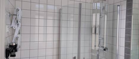 Une salle de bain moderne avec une douche à parois de verre, des murs recouverts de carreaux blancs et un lavabo blanc.