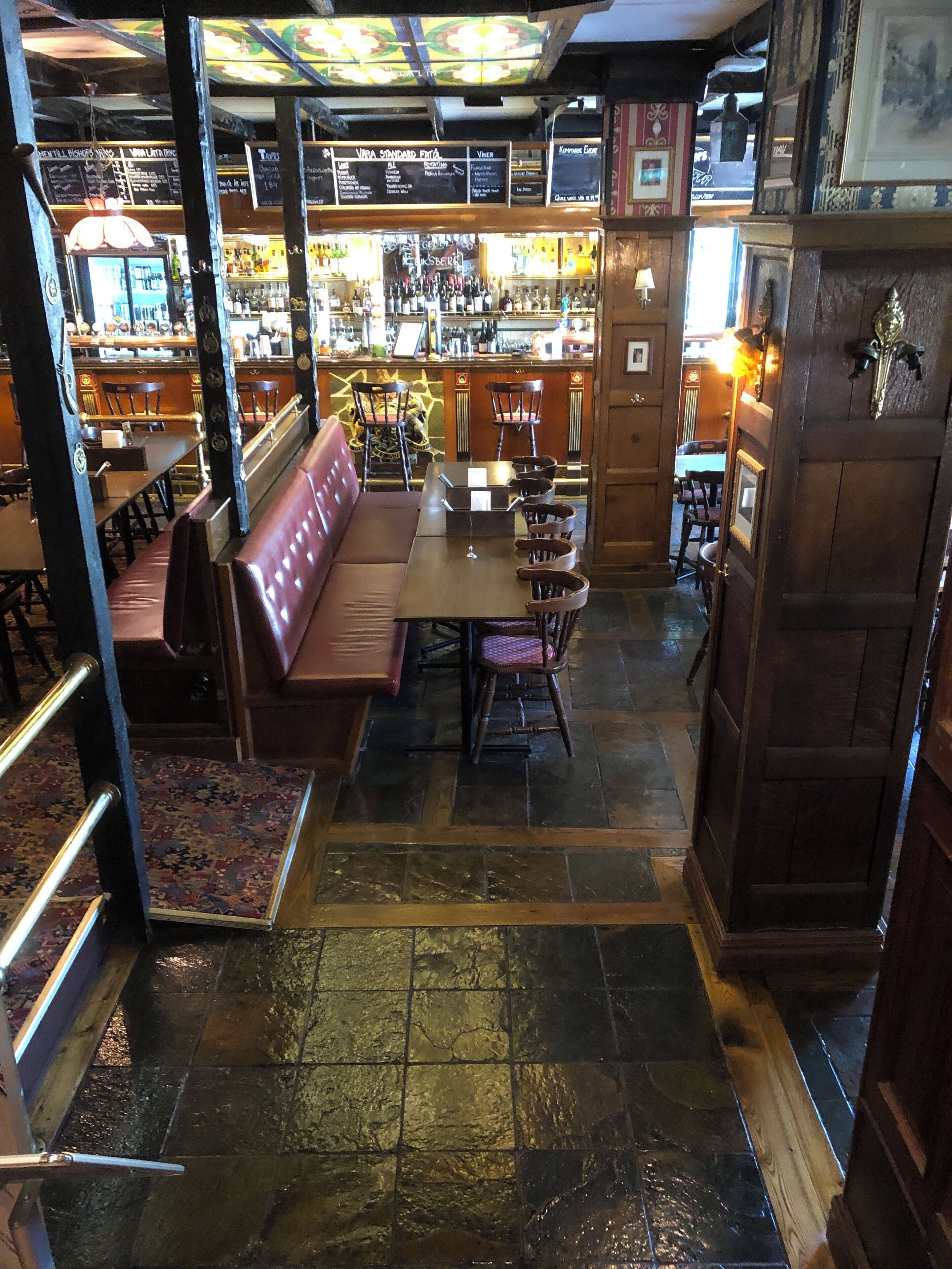 Una zona de bar con barra, taburetes y un espacio de asientos con banco y sillas.