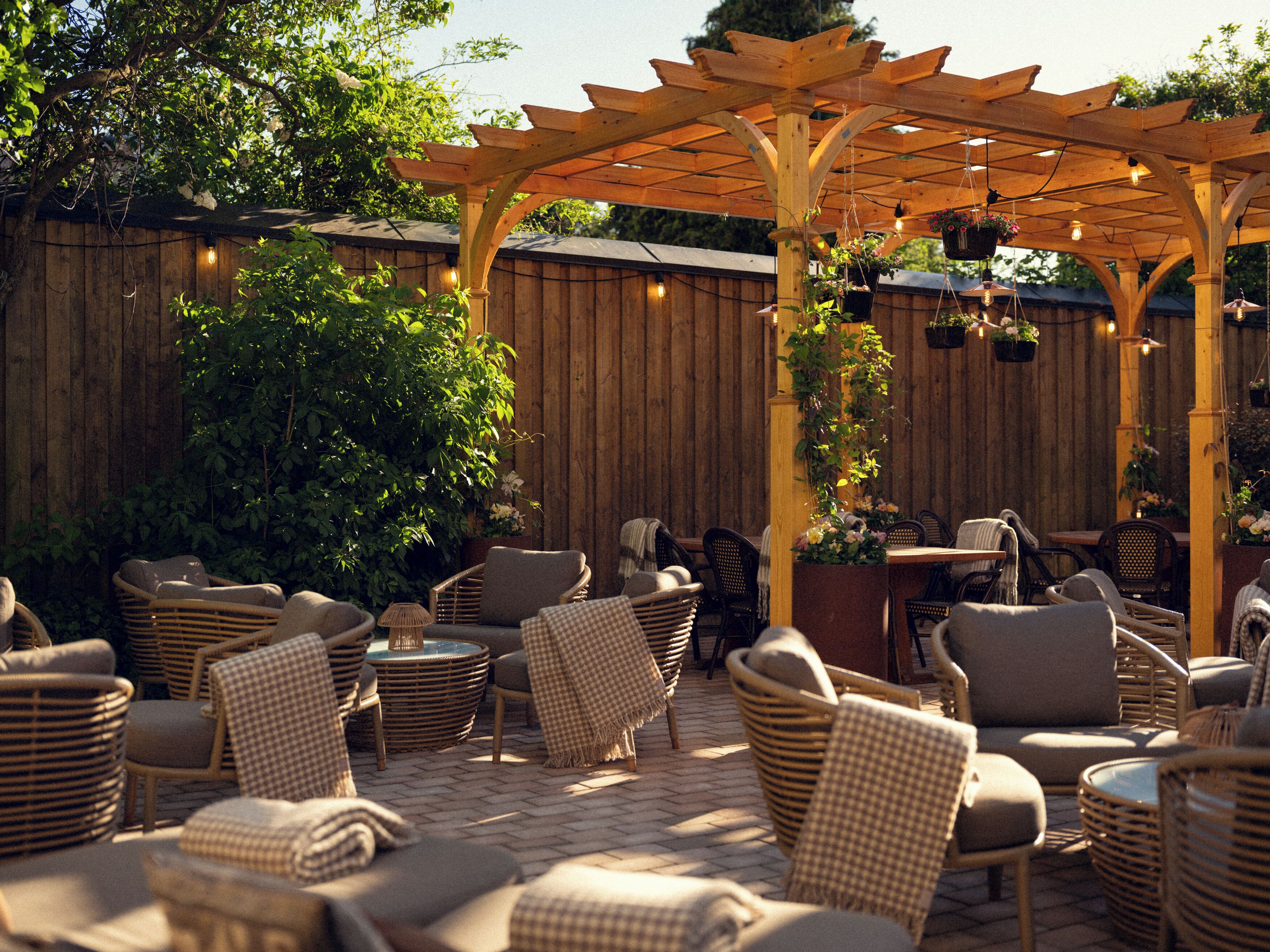 Un patio con mobiliario de mimbre, una pérgola y plantas colgantes.