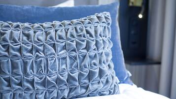 A close-up of a tufted pillow with a geometric pattern, placed on a bed with a white sheet.