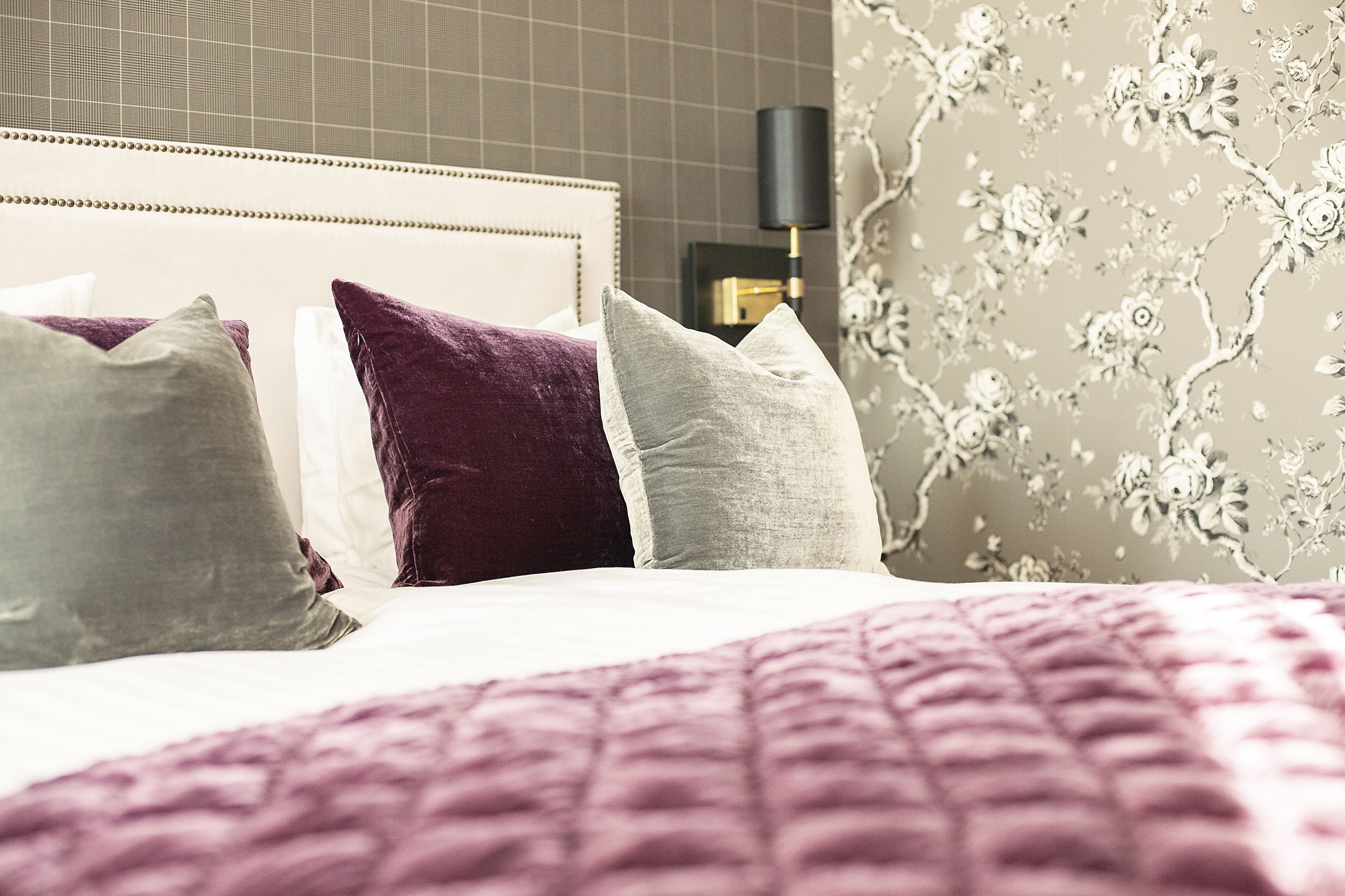 A neatly made bed with a purple blanket and multiple pillows in shades of purple and grey.