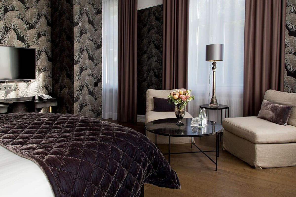 A hotel room with a large bed, a sofa, a small table with a vase of flowers, and a lamp.