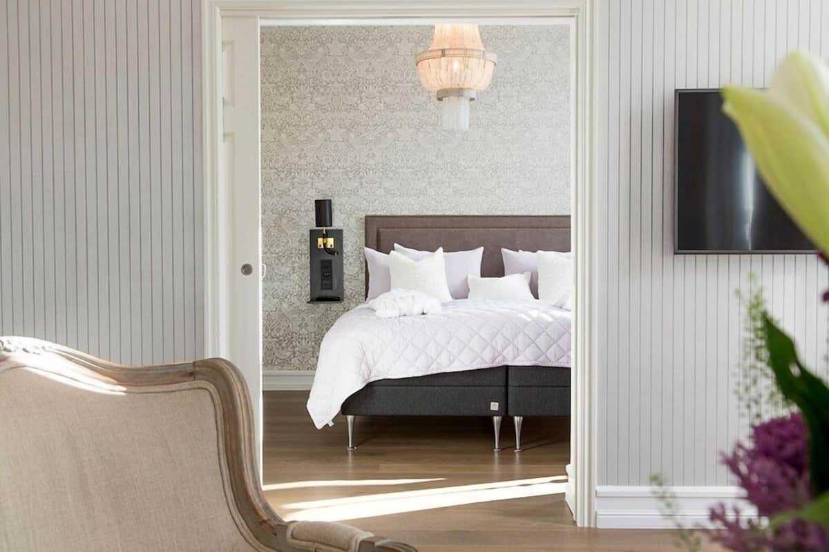 A bedroom with a bed, a nightstand, a wall-mounted TV, and a chandelier.