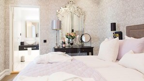 A hotel room with a large bed, a vanity with a mirror, a nightstand with a lamp, and a view of the bathroom. - Continental du Sud (Ystad)