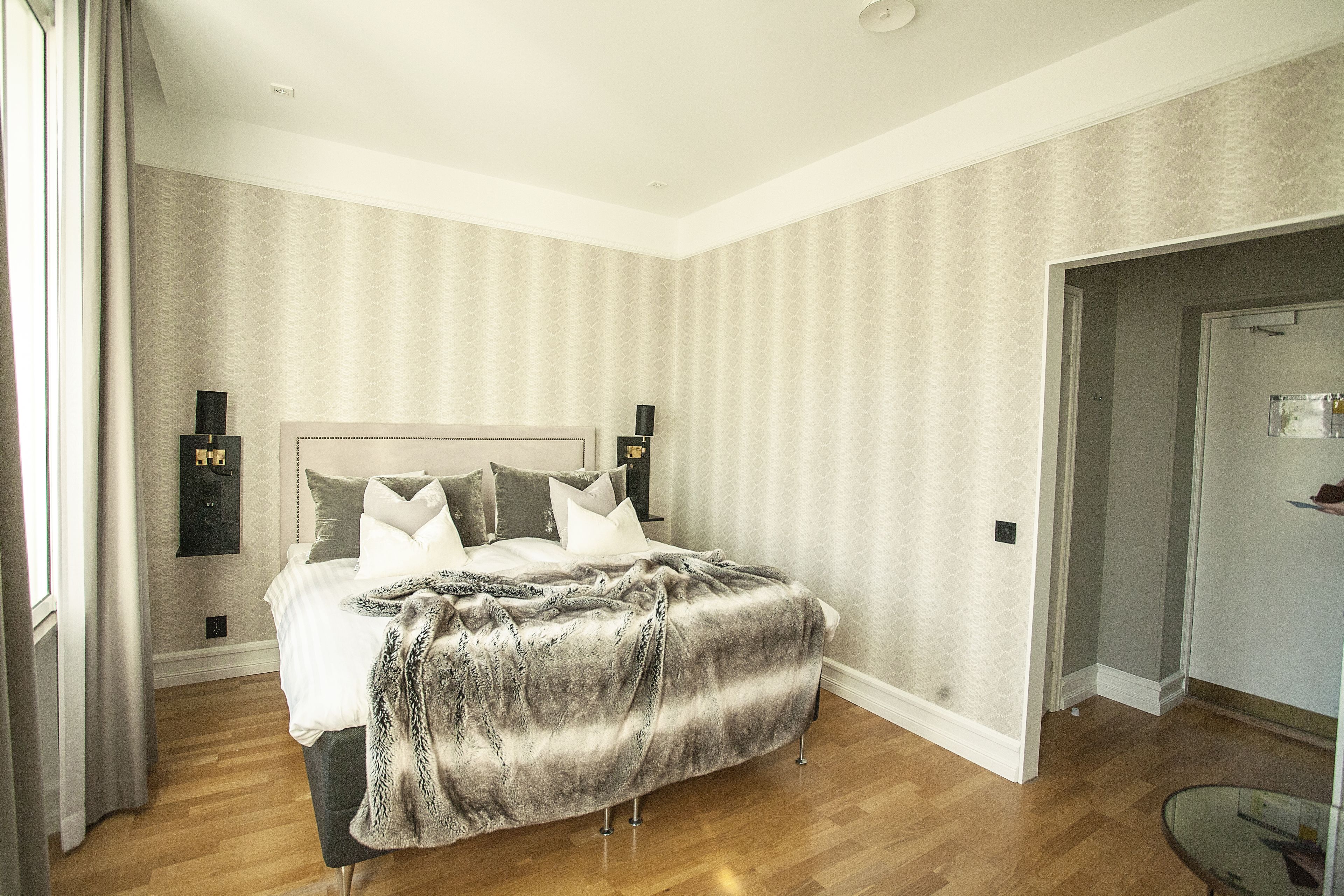 A bedroom with a large bed, wooden flooring, and a patterned wallpaper.