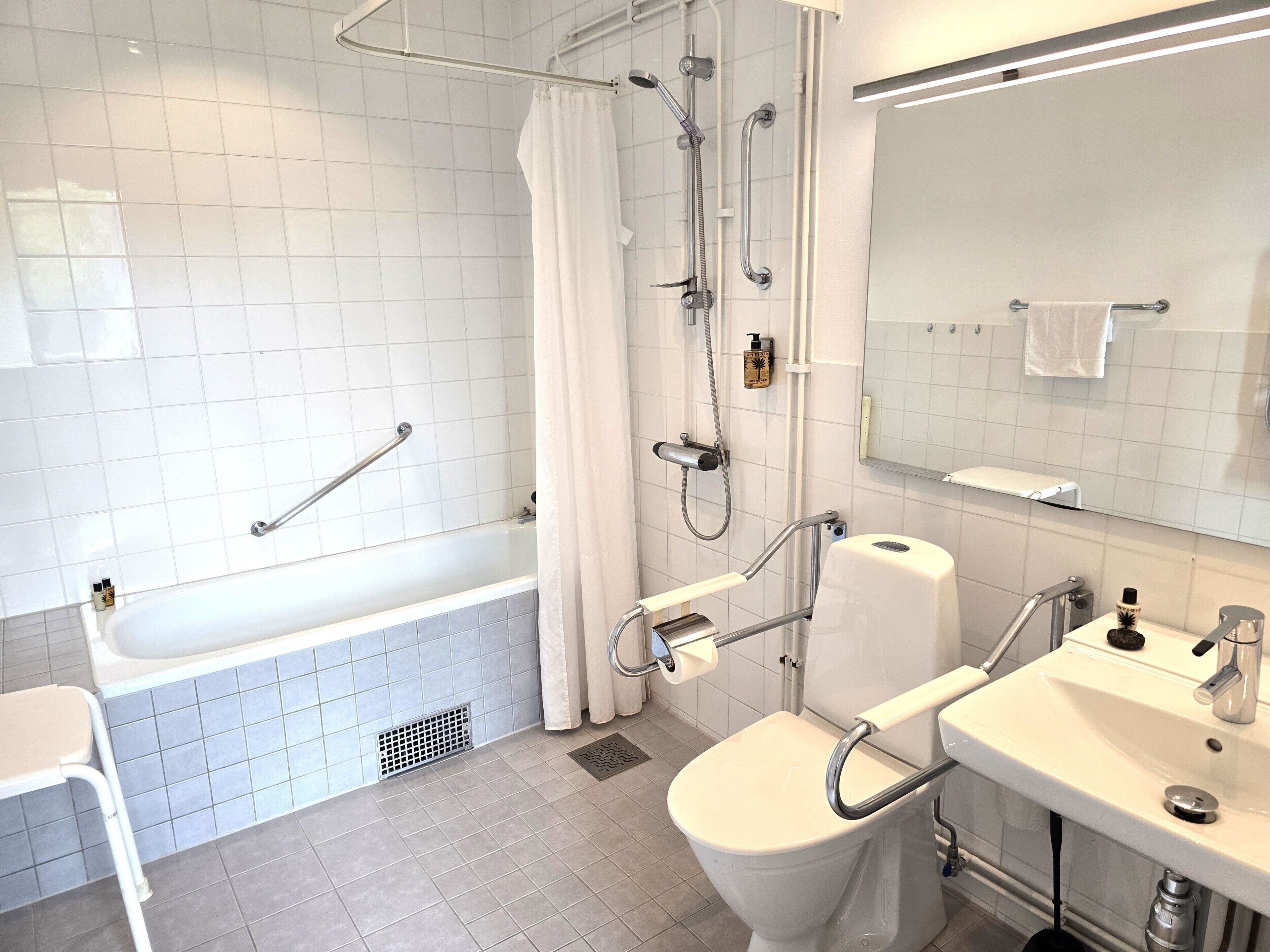 A modern bathroom with a bathtub, toilet, and sink, equipped with grab bars and a shower head.