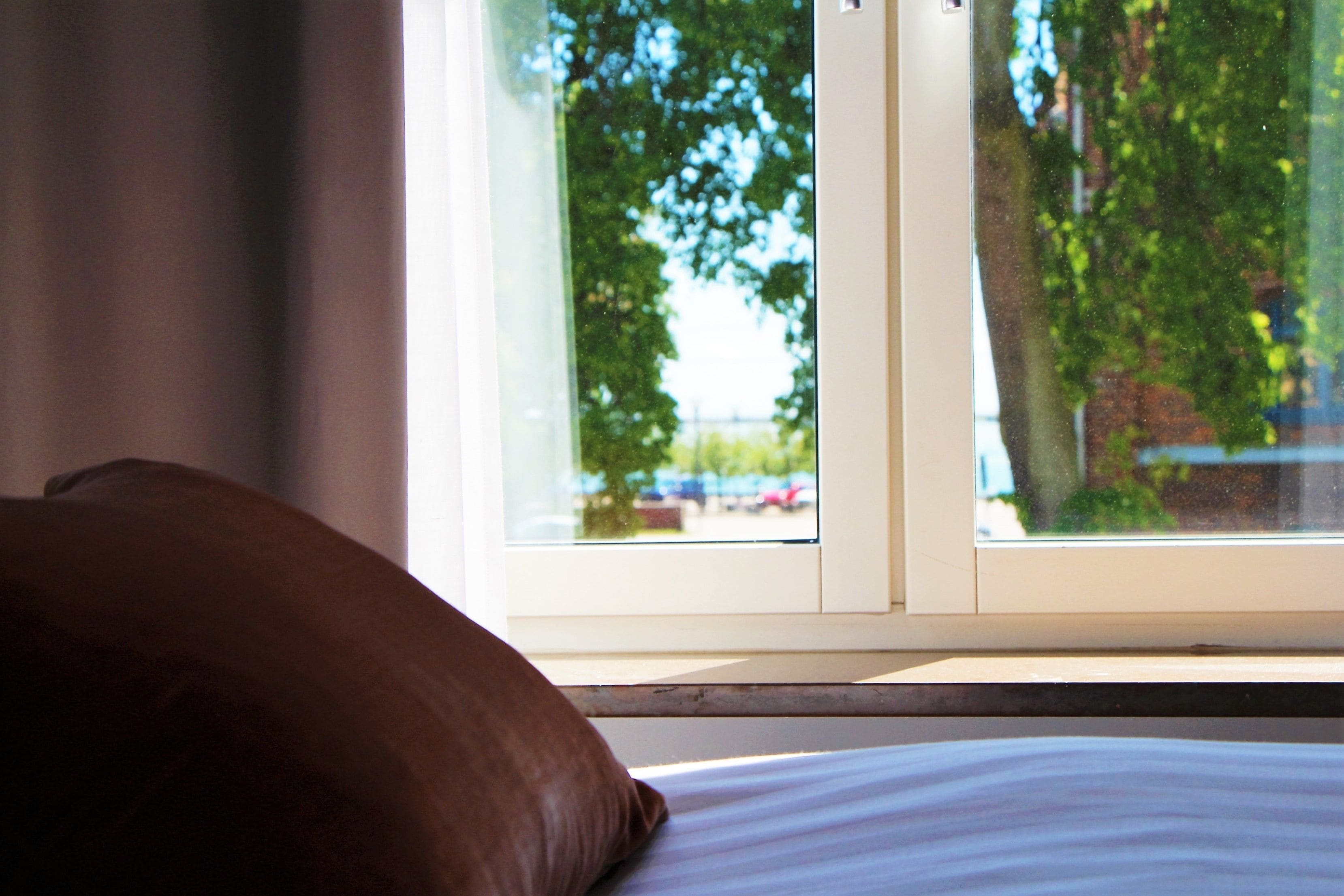 Ein Bett mit Kissen und einem Fenster mit Blick auf Bäume und geparkte Autos.