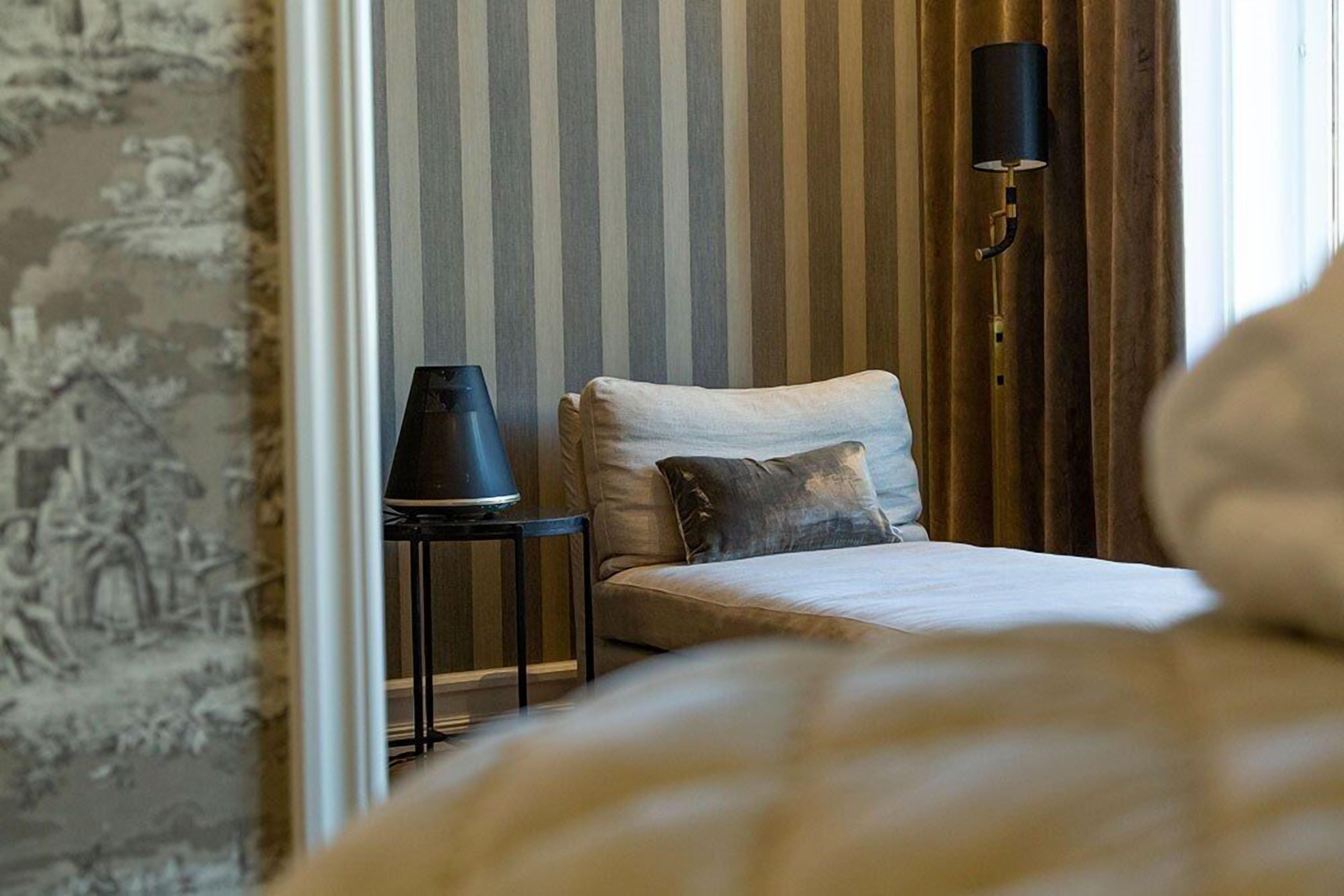 A bedroom with a bed, a nightstand, a lamp, and a striped wall.