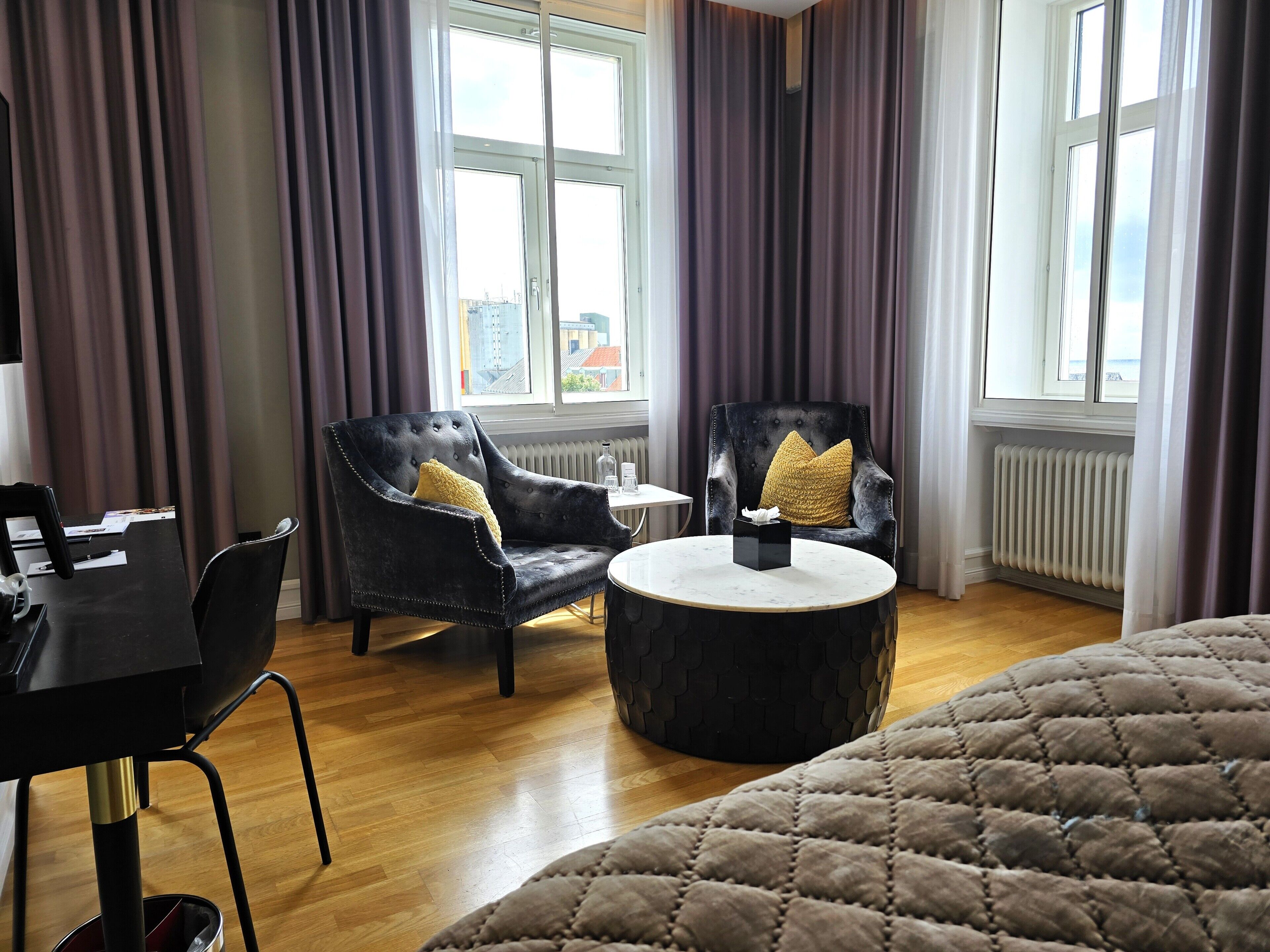 A hotel room with a bed, two armchairs, a small round table, and a radiator.