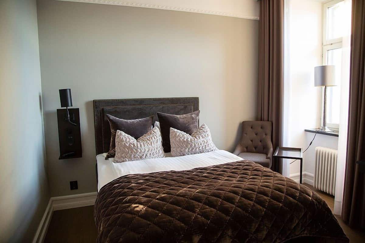 A neatly made bed with a brown quilt, a dark headboard, and two decorative pillows.