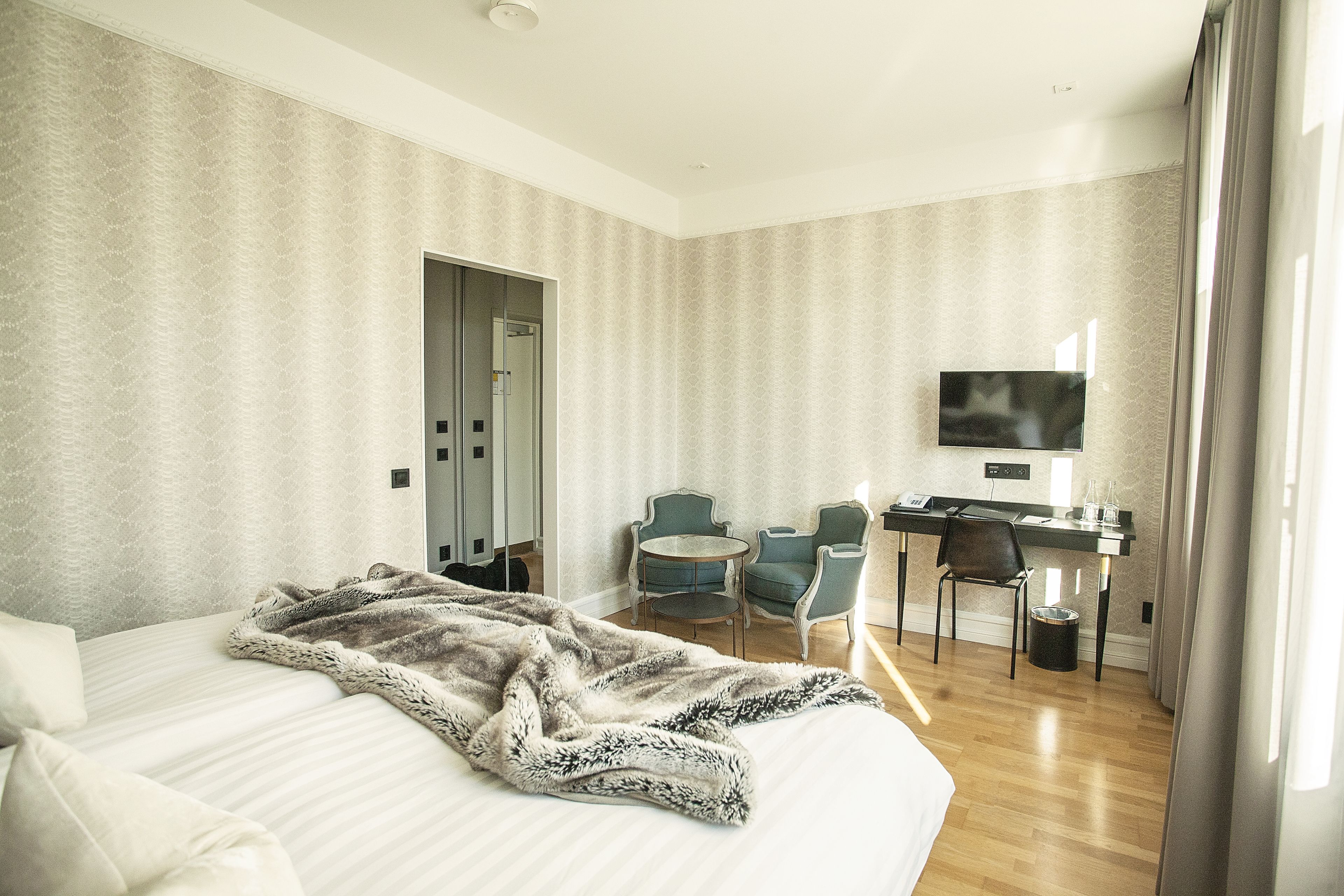 Une chambre d’hôtel avec un lit, un bureau, deux chaises, une télévision et une porte.