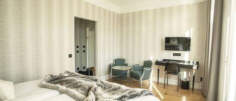 Une chambre d’hôtel avec un lit, un bureau, deux chaises, une télévision et une porte.