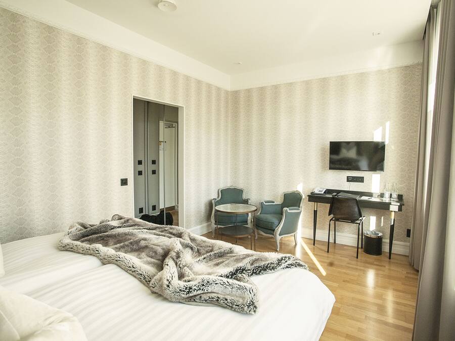 A hotel room with a bed, a desk, two chairs, a television, and a door.