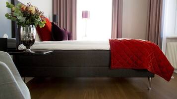 Un dormitorio moderno con una cama color gris oscuro, una colcha acolchada roja y un jarrón de flores en la mesita de noche.