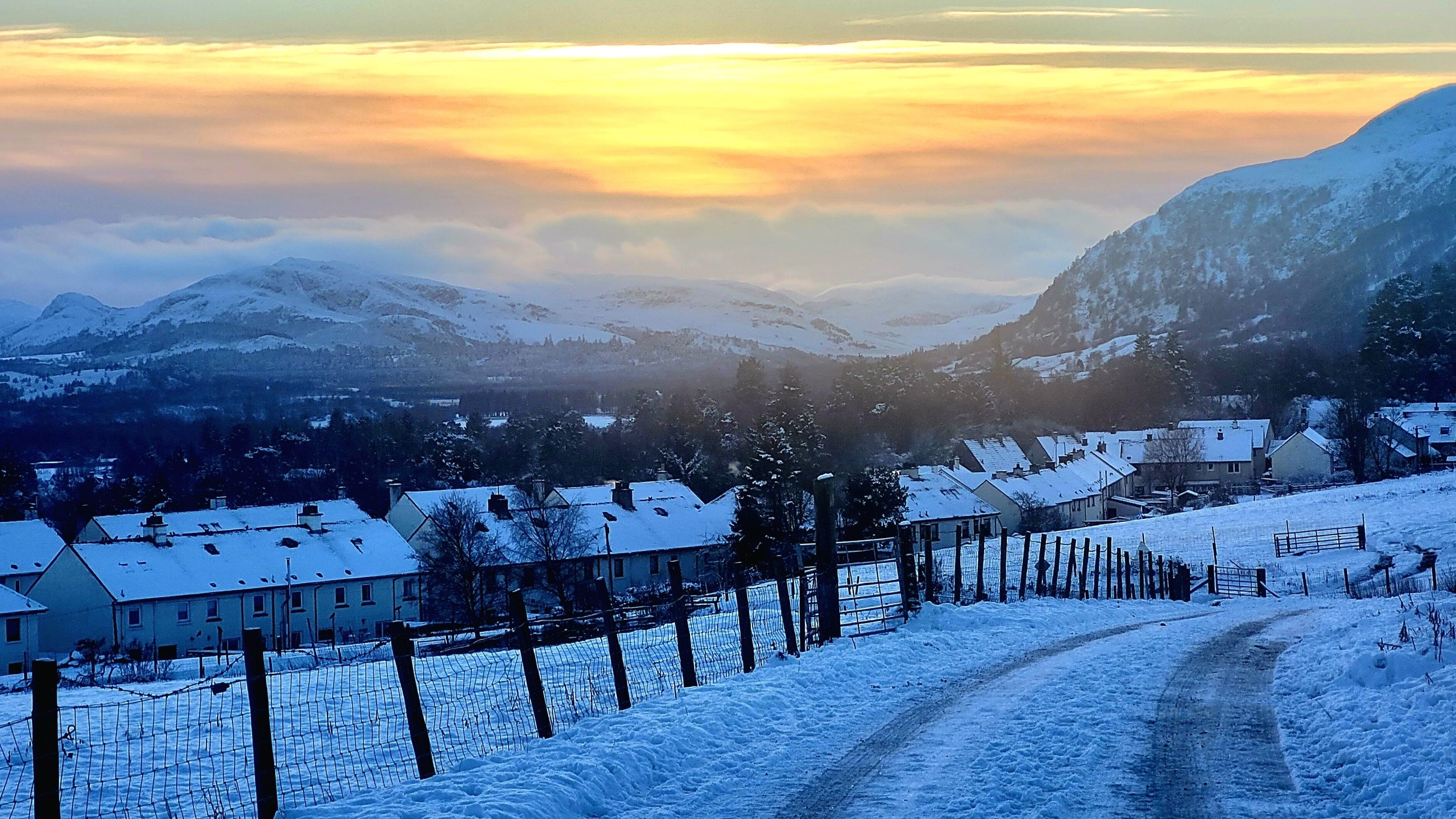 A snow-covered landscape with a mountain in the background and a road leading into a village.