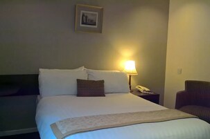 Una habitación de hotel con una cama bien tendida, una lámpara de noche, un teléfono y un cuadro en la pared.
