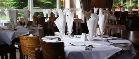 Un restaurante con mesas redondas dispuestas con manteles blancos, cubiertos y servilletas.