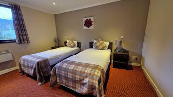 A hotel room with two beds, a window with curtains, a wall-mounted flower decoration, and a red carpeted floor.