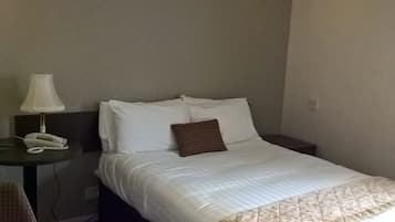 A hotel room with a bed, a bedside table with a lamp, a phone, and a chair.
