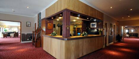 A reception area with a wooden counter, red patterned carpet, and a staircase leading to another floor.