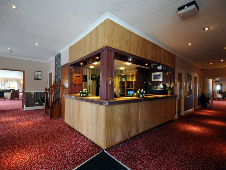 Un espace d’accueil avec un comptoir en bois, un tapis à motifs rouges et un escalier menant à un autre étage.