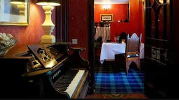 A room with a piano, a table set for dining, and a patterned carpet.