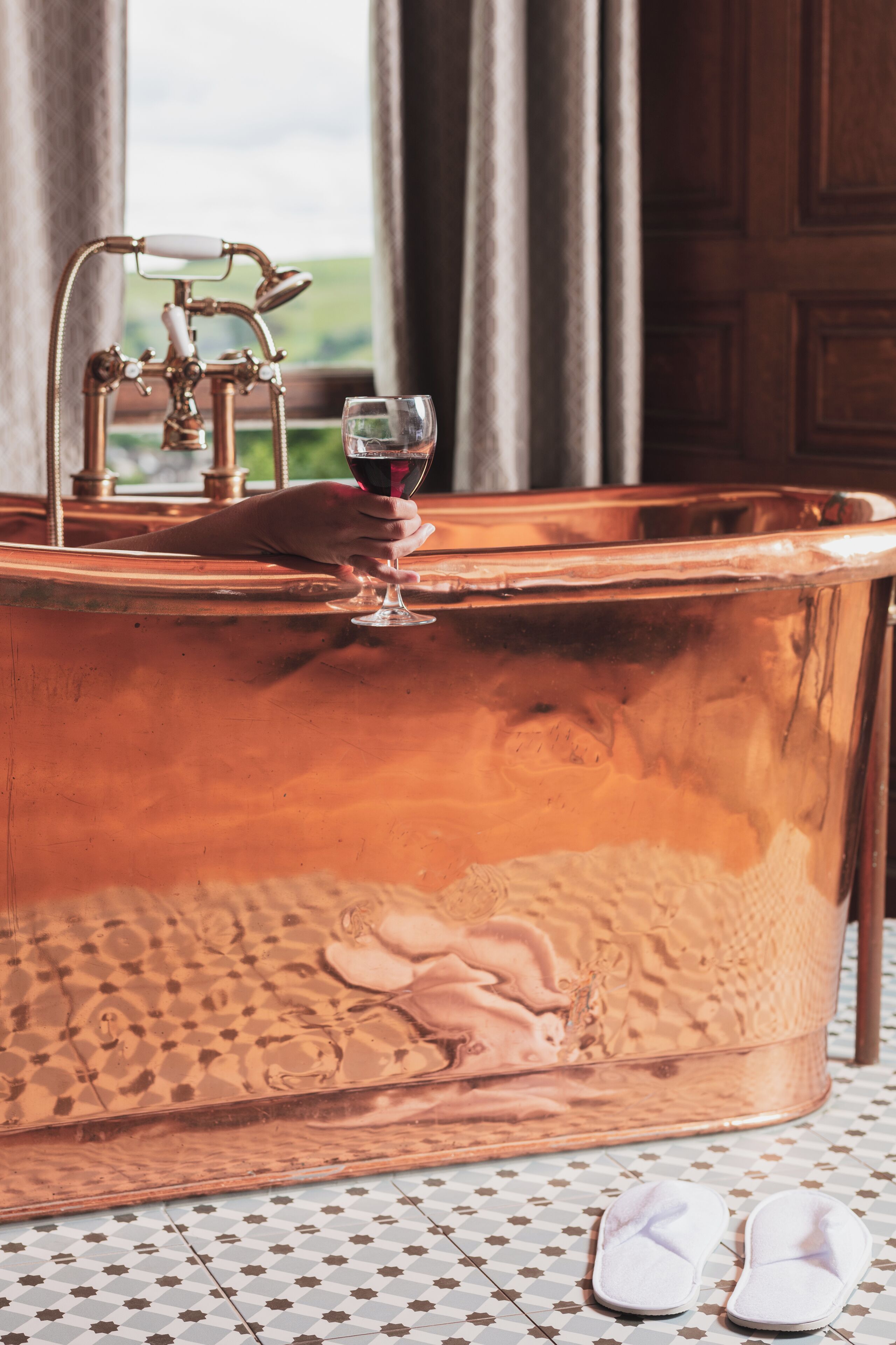 A copper bathtub with a faucet and a wine glass.