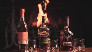 Three bottles of whisky and four glasses on a wooden table with a fireplace in the background.
