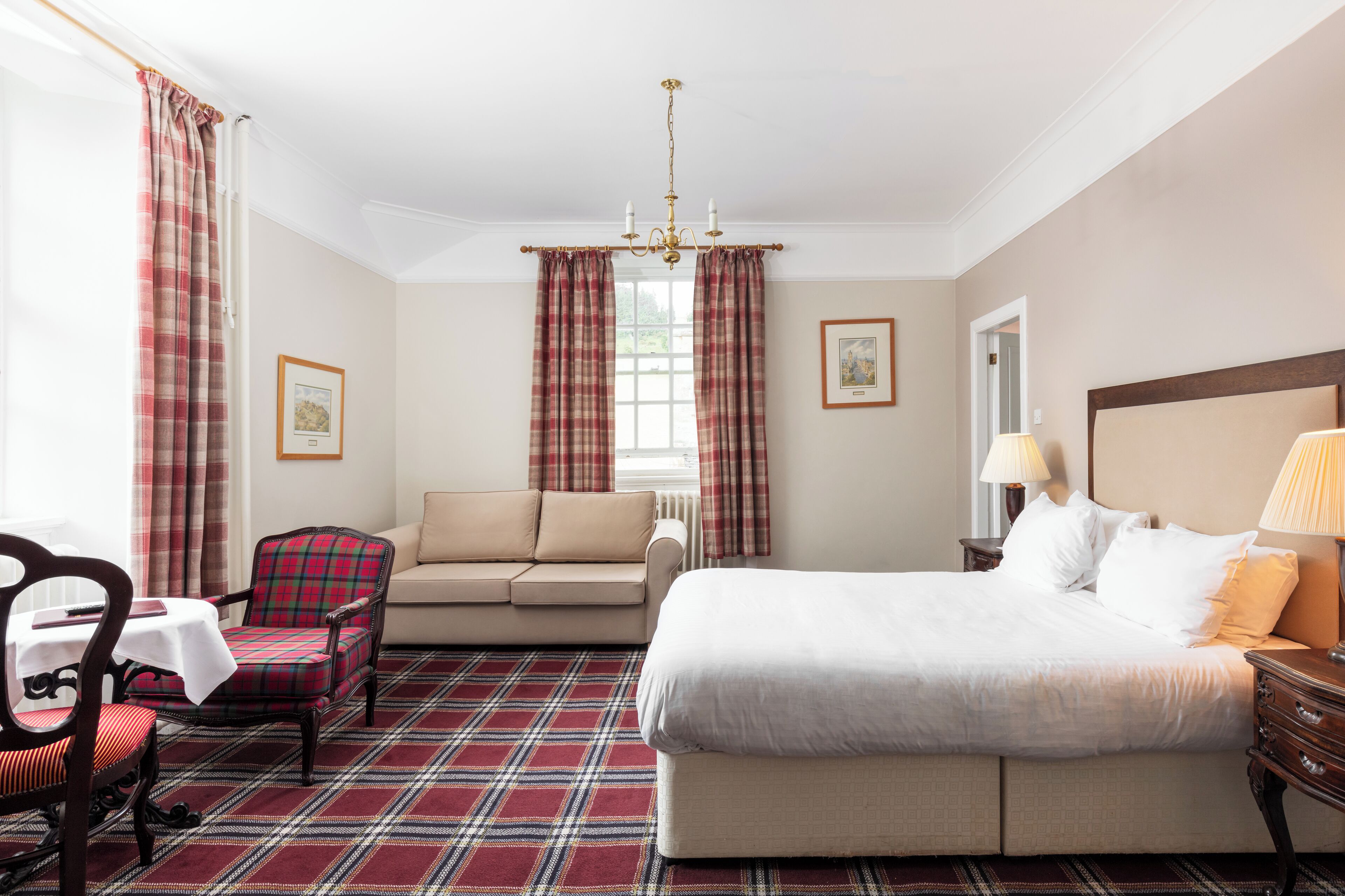 Habitación de hotel con cama, sofá, sillón, mesa y ventana con cortinas.