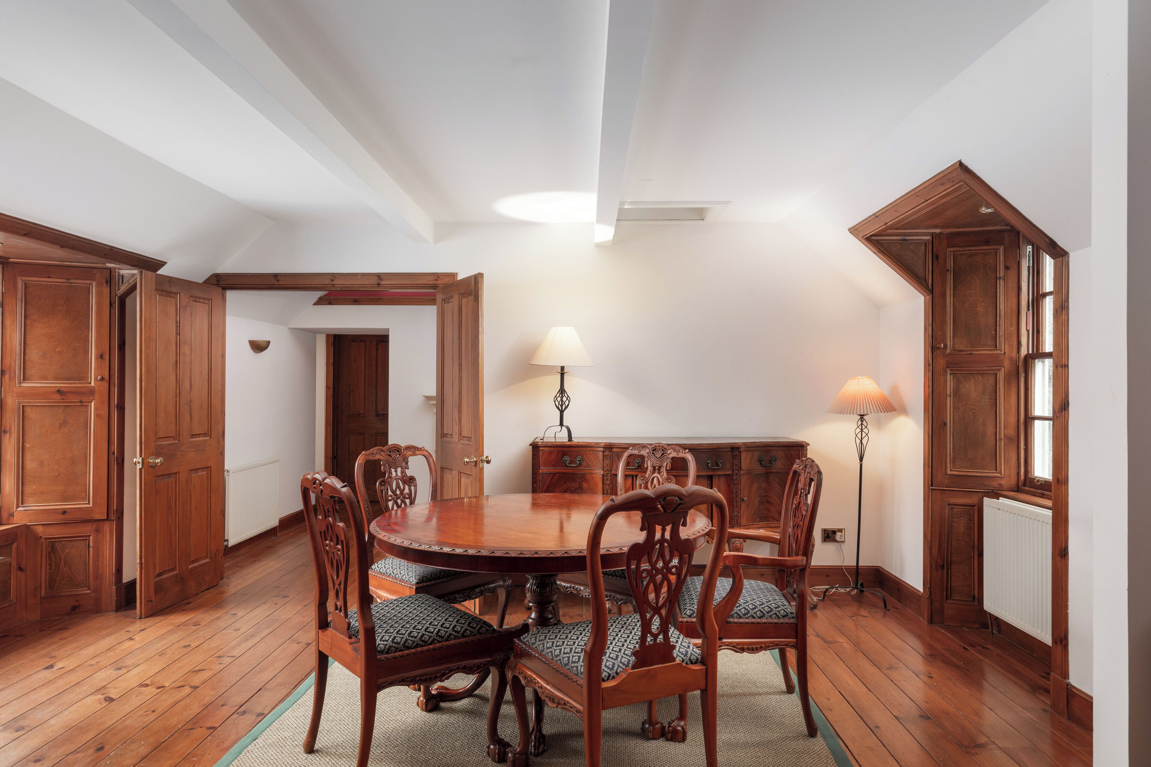 A dining room with a wooden table and chairs, a lamp, and wooden cabinets.
